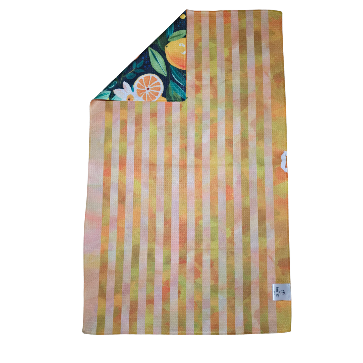 Reverse side of a double-sided waffle weave microfiber hand towel with vertical orange and yellow stripes, with a folded corner showing the navy citrus and floral patterned front.