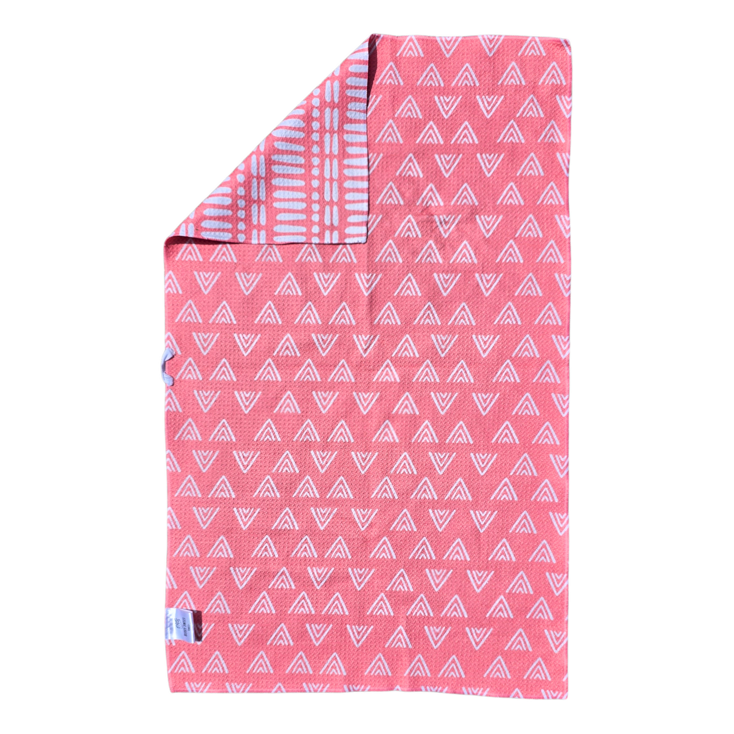 Bright pink waffle weave microfiber hand towel laid flat, showing the reverse side with white triangular geometric patterns and a folded corner revealing the white line and dot patterned front.