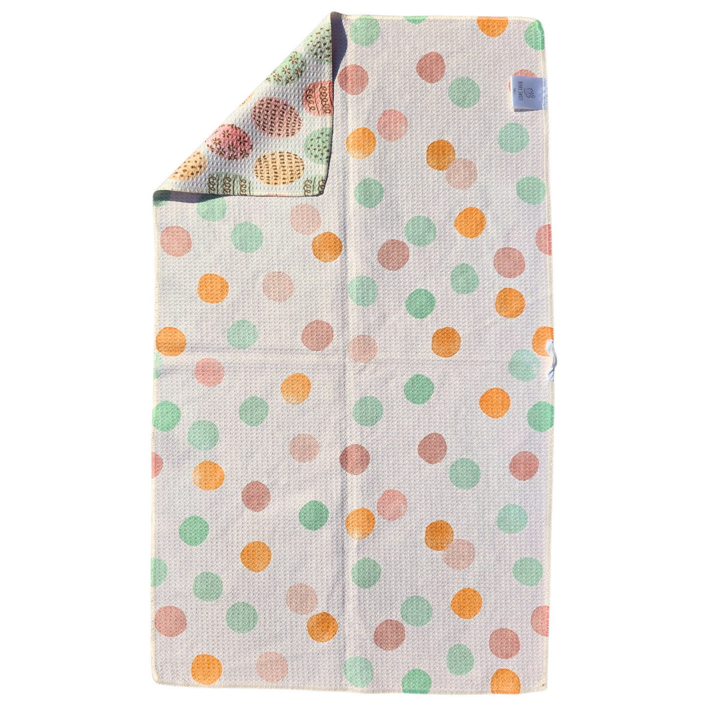Full view of pink, mint green and peach polka dot pattern on a cream microfiber waffle weave towel, with one corner folded to reveal the reverse side featuring coordinating pastel Easter egg designs.