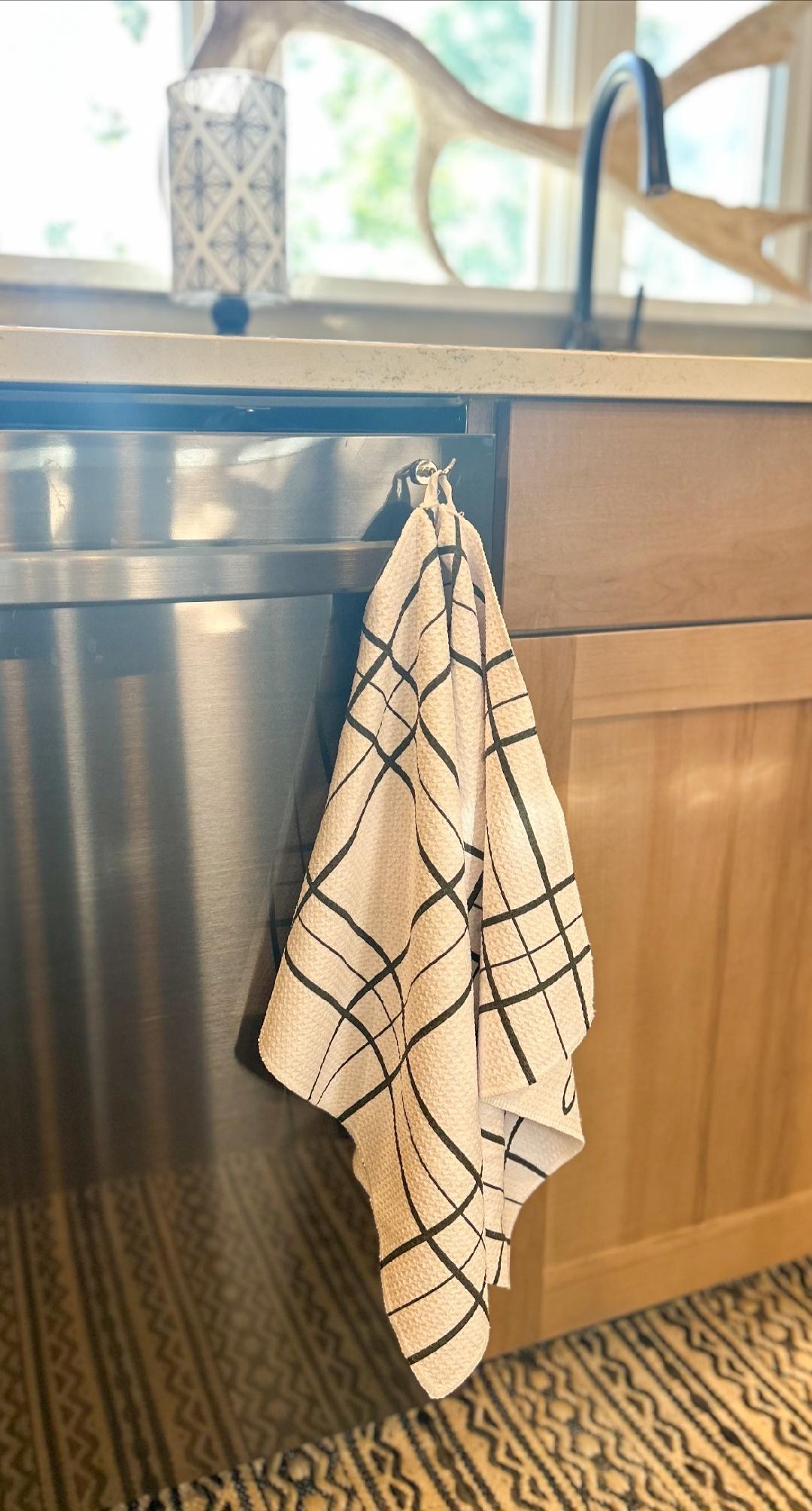 Back view of a single microfiber hand towel with a white background and black grid pattern hanging from the hang loop on a dishwasher in an aesthetic kitchen.
