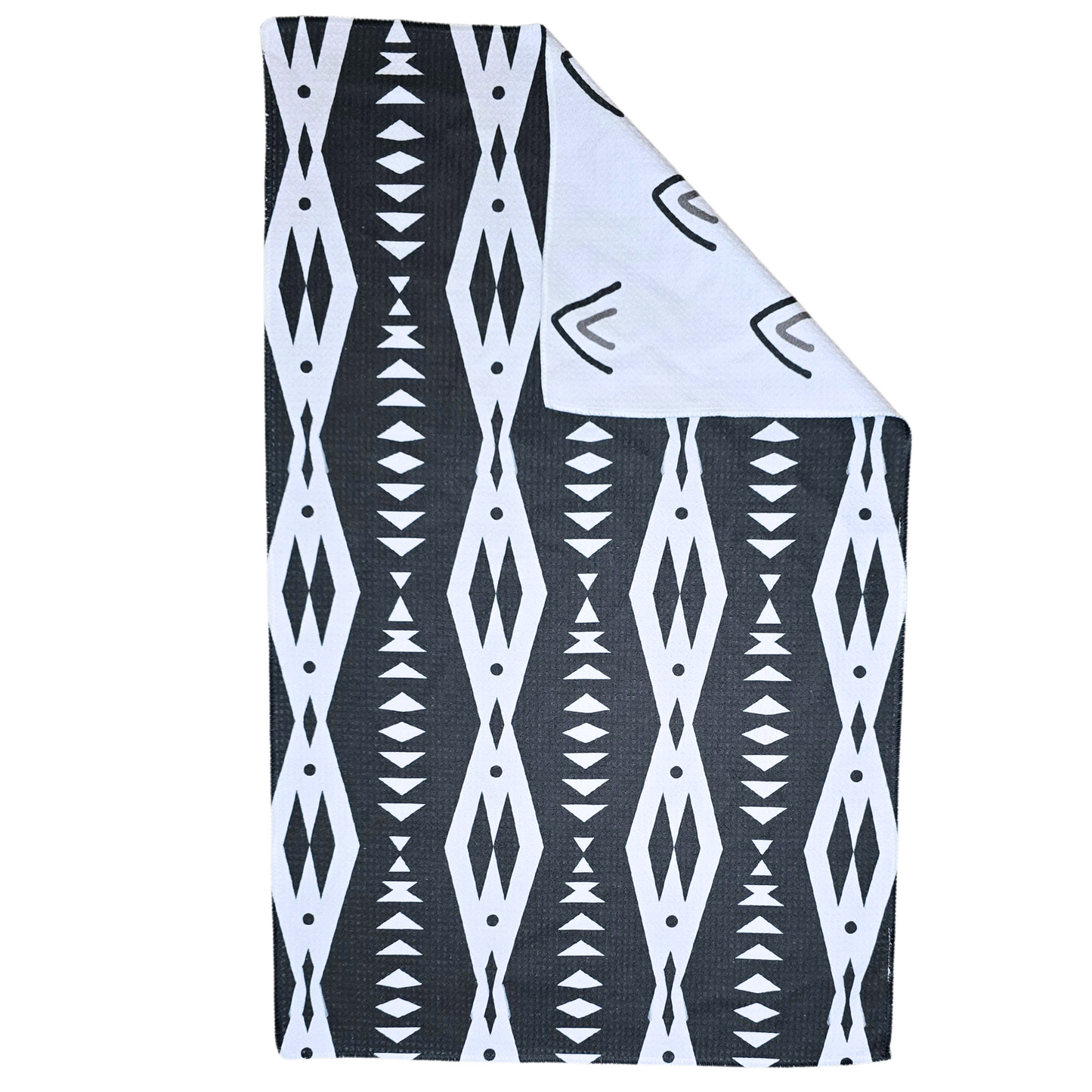 Double-sided waffle weave microfiber hand towel laid flat, featuring a black background with repeating white geometric diamond and triangle patterns and a folded corner revealing the white reverse side with black and gray arrow style triangle designs.