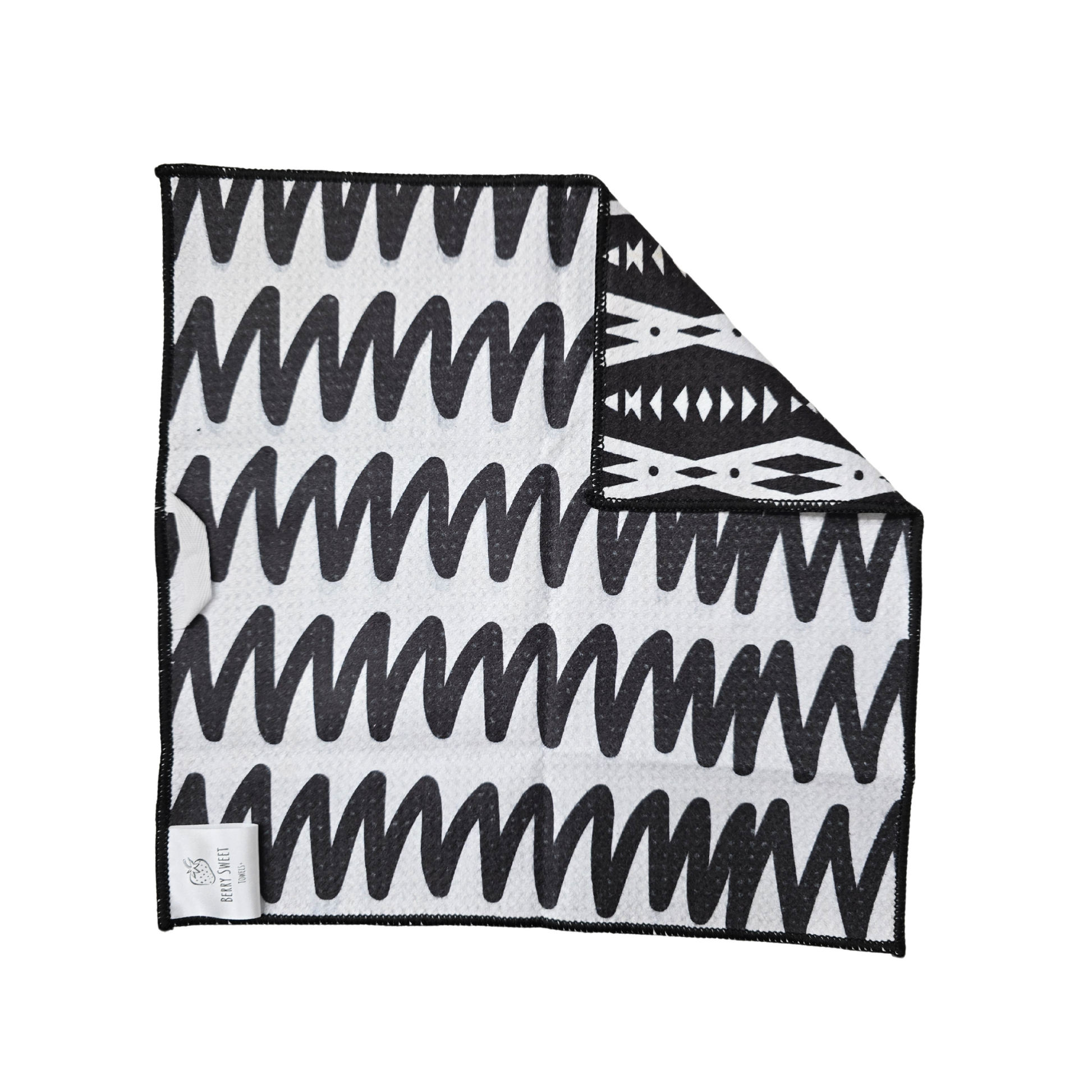 Black and white waffle weave microfiber washcloth laid flat with a folded corner, showing the zigzag lined front and contrasting reverse side with geometric shapes.