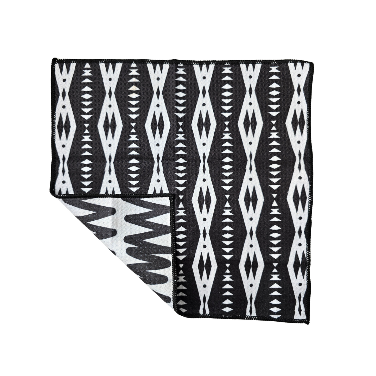 Black and white waffle weave microfiber washcloth laid flat with a folded corner, showing the geometric patterned front and contrasting reverse side with zigzag lines.