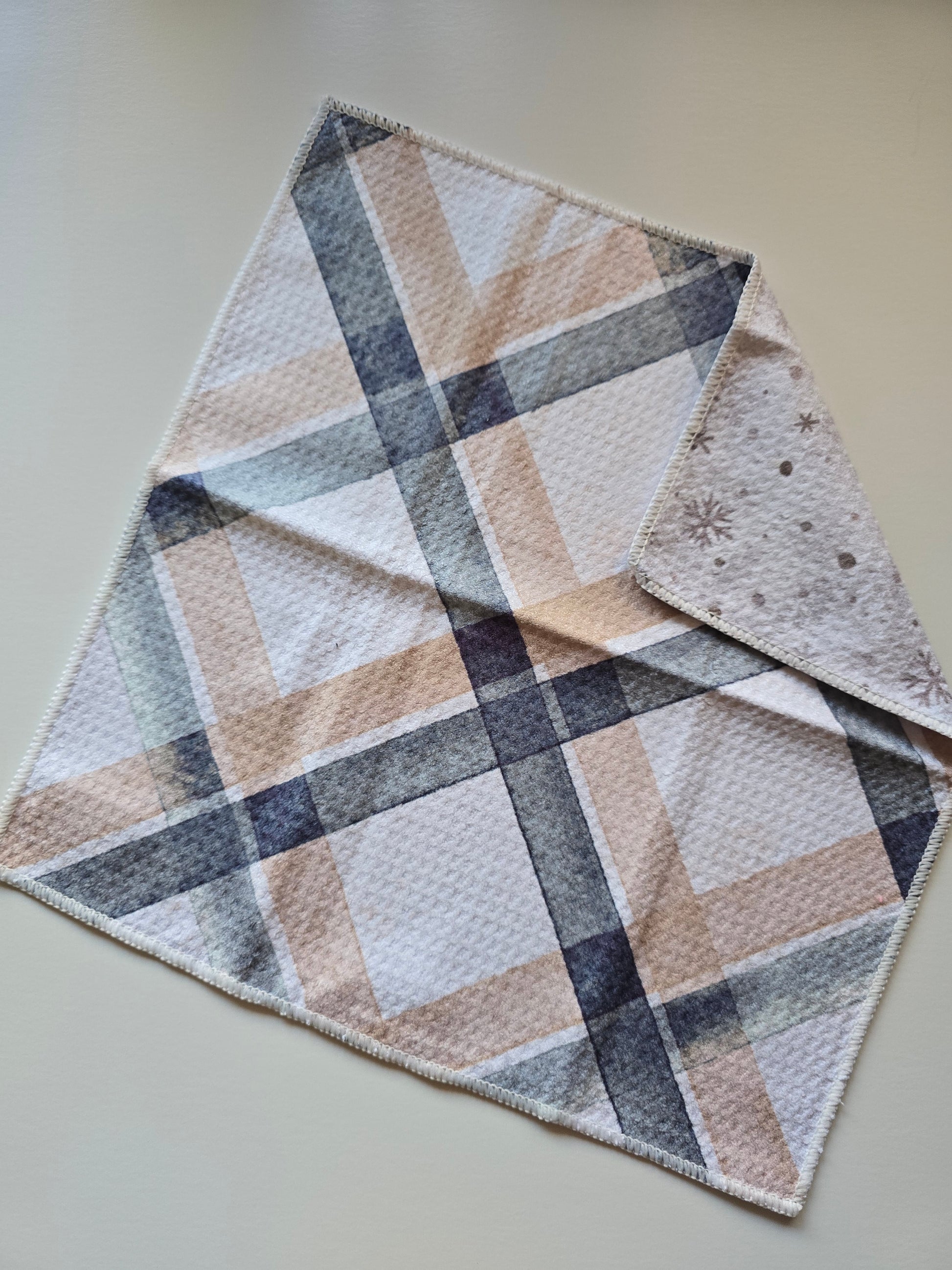 Single waffle weave microfiber washcloth folded to show both sides, with a blue and tan plaid patterned front on a plain background and a cream and silver background reverse with gold snowflake pattern.