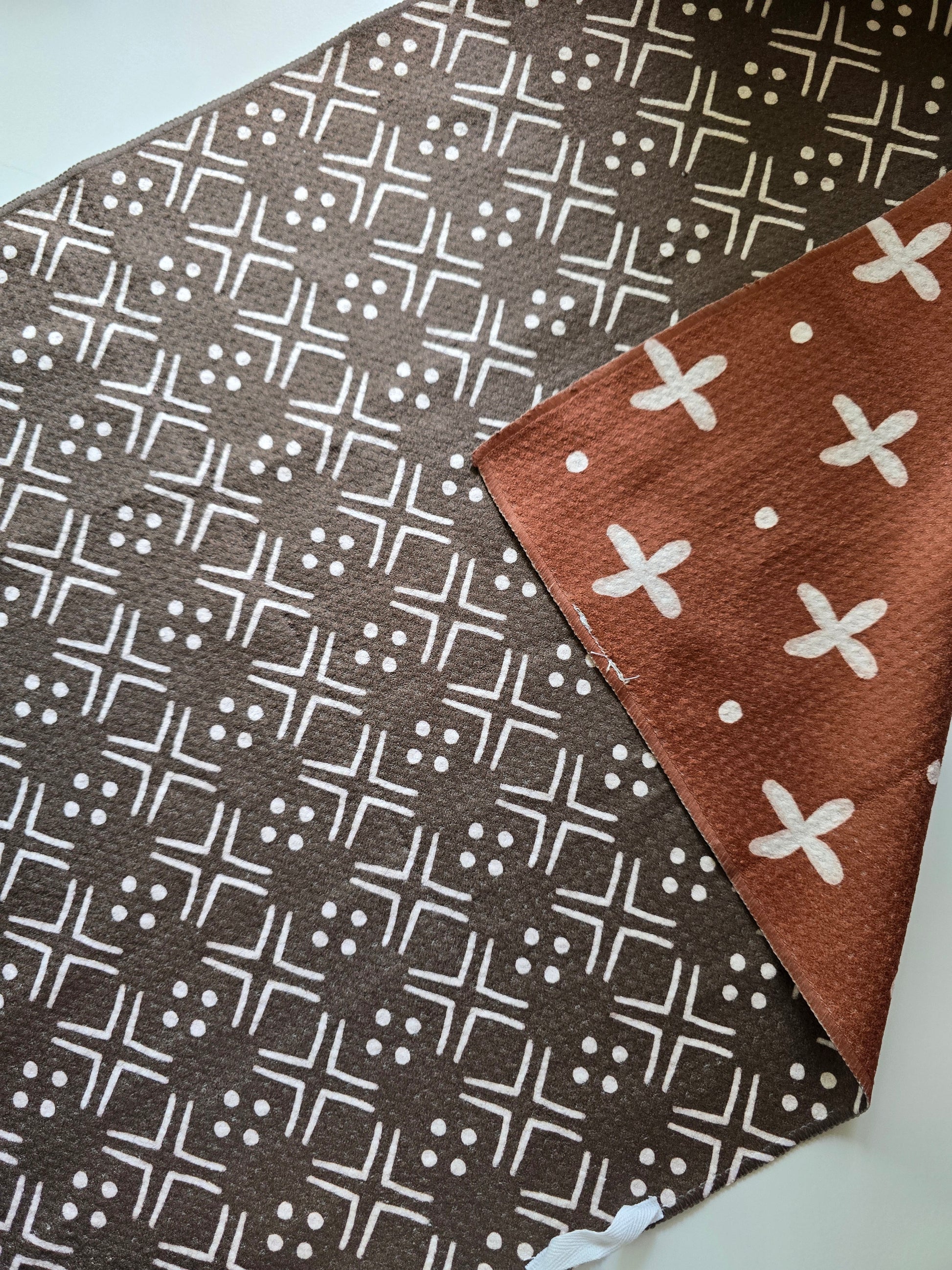 Double-sided waffle weave microfiber hand towel showing dark brown colored with white geometric patterned side with folded corner revealing rust-colored reverse side with white cross and dot pattern.