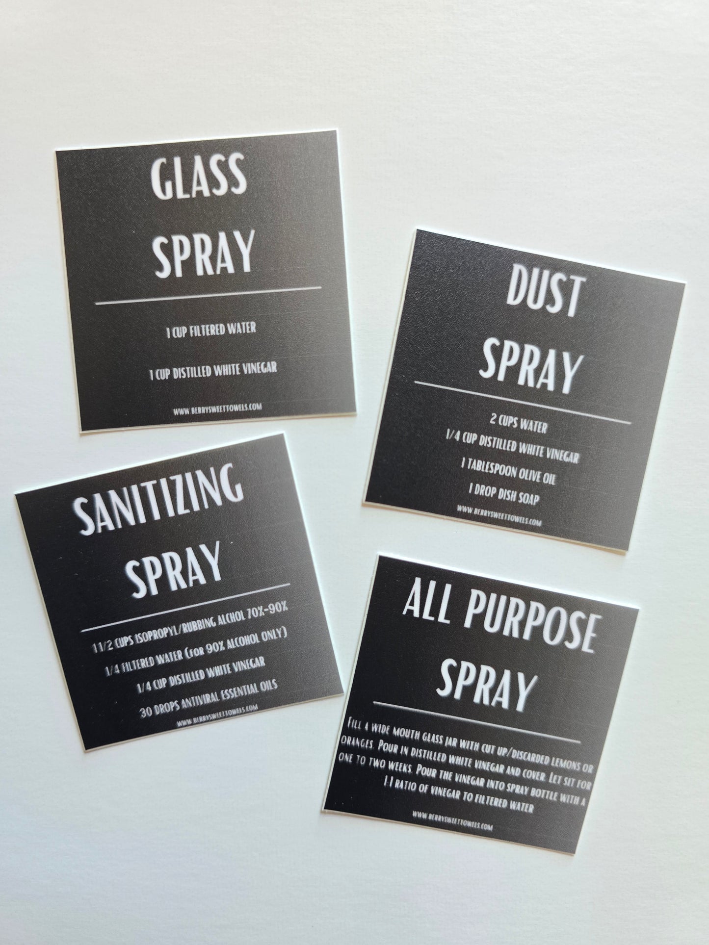 Set of four square mini vinyl stickers featuring DIY cleaning spray recipes in white text on black backgrounds, labeled Glass Spray, Dust Spray, Sanitizing Spray, and All Purpose Spray.