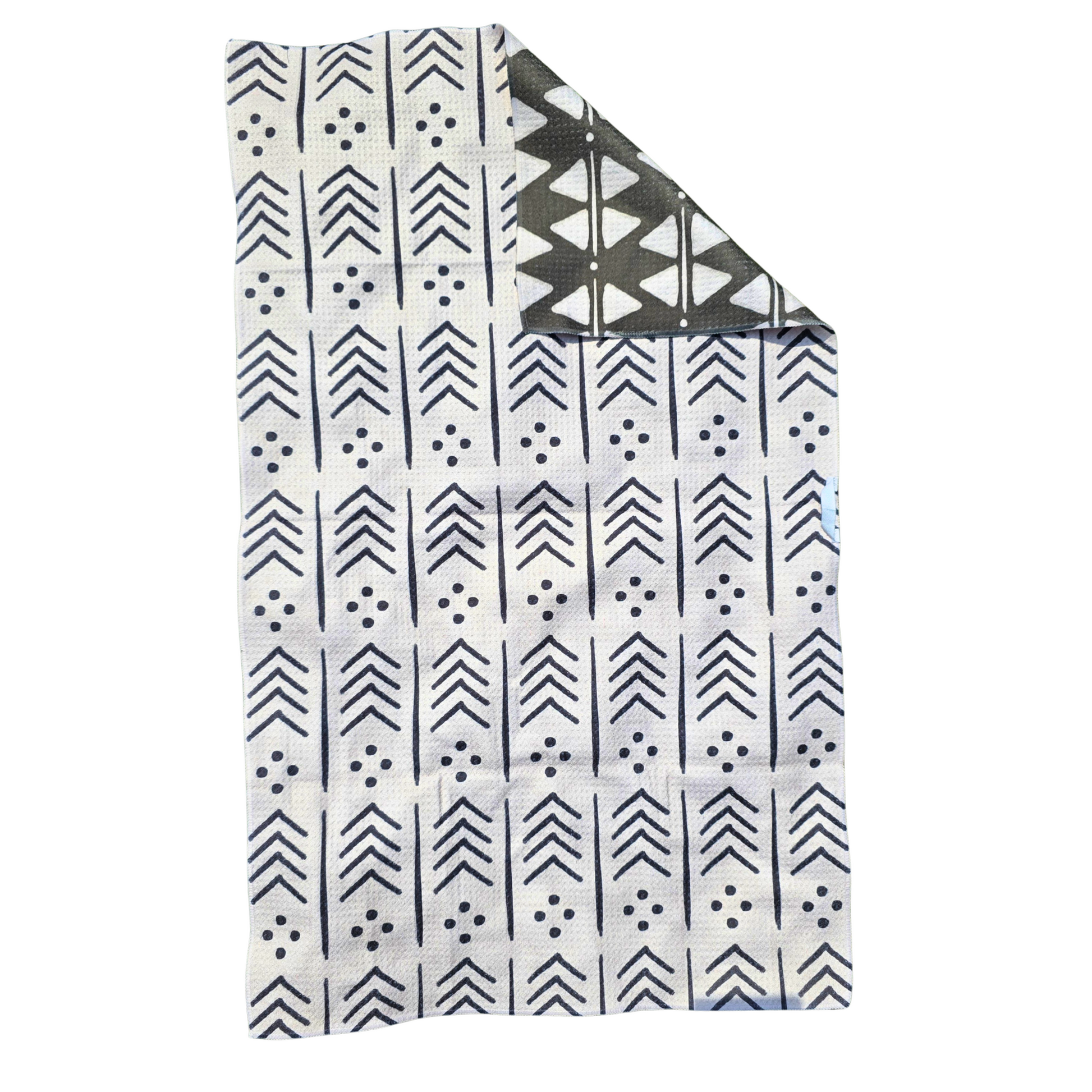 Full view of a single microfiber towel with a corner folded over to reveal the reverse side. This is showing the backside of the towel. The back is a light cream background with black arrow, line and dot designs, while the folded corner shows the black reverse side with white triangle, dot and line patterns.