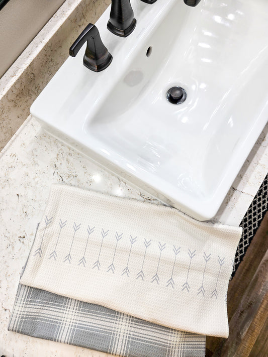 Single waffle weave microfiber hand towel displayed as two folded sections on a bathroom countertop beside a sink, showing a cream front with rows of gray arrow pattern and a gray and cream plaid reverse side.