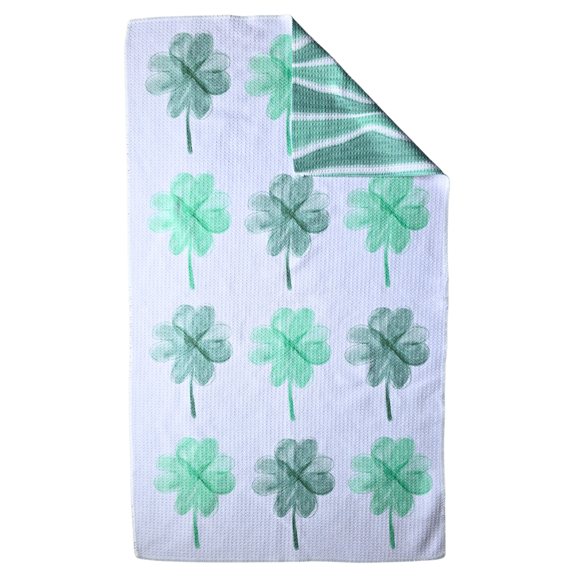Double-sided waffle weave microfiber hand towel laid flat, showing a white background with repeating dark and light green four leaf clovers in varying shades, with a folded corner revealing the light and dark green and white wavy stripe reverse side.