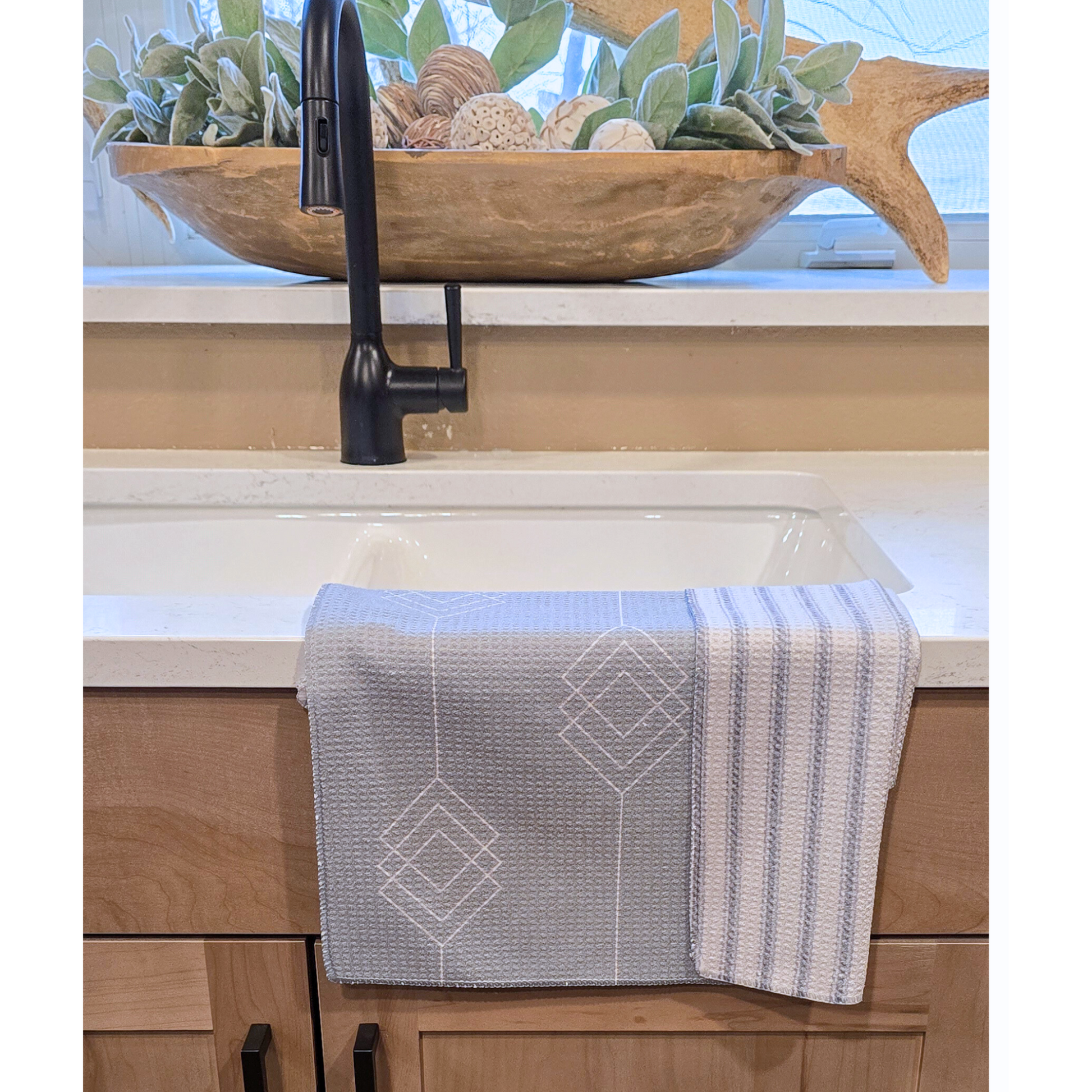 Single waffle weave microfiber hand towel folded over a kitchen sink, showing a light gray background with white geometric diamond patterned front and a light and dark gray striped reverse.