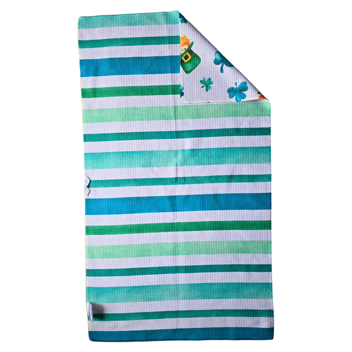 Reverse side of a double-sided waffle weave microfiber hand towel featuring green and teal horizontal stripes on a white background, with a folded corner displaying the shamrock and leprechaun patterned front.
