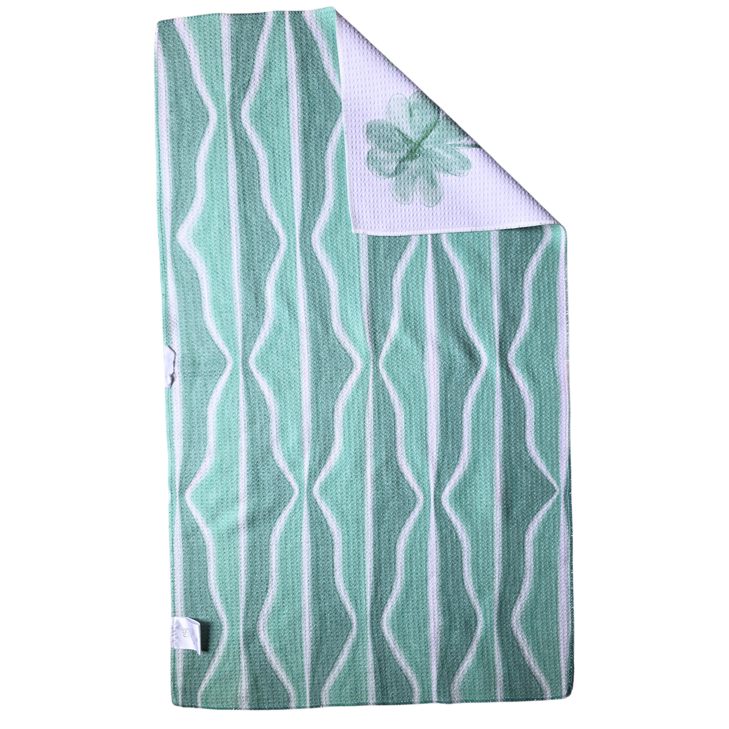 Reverse side of a double-sided waffle weave microfiber hand towel featuring a light and dark green background with white wavy vertical stripes, with a folded corner displaying the white four leaf clover patterned front.