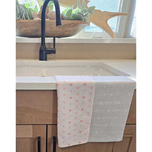 Waffle weave Towel draped over a kitchen sink, showing a white front with small multicolored heart patterns and a soft blue reverse side with white repeating “love” text and small heart designs.