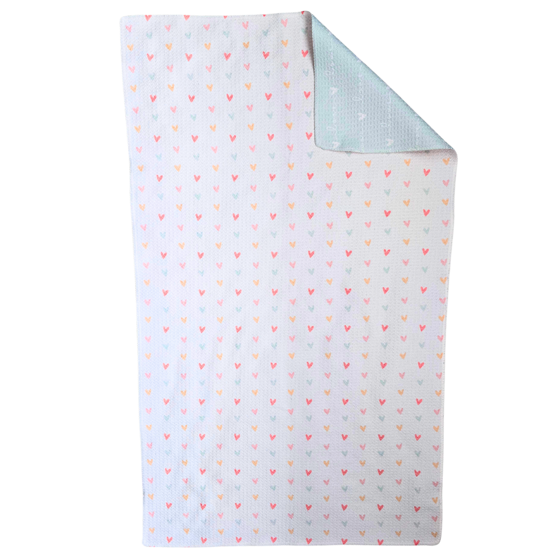Waffle weave microfiber Towel laid flat with the front side visible, featuring a white background covered in small multicolored hearts, with one corner folded to reveal the soft blue reverse side printed with repeating “love” text and hearts.