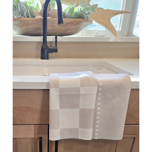 Double-sided waffle weave microfiber hand towel draped over a white kitchen sink, showing a beige and white checkered front and a light beige reverse side with vertical square dotted stripe details.