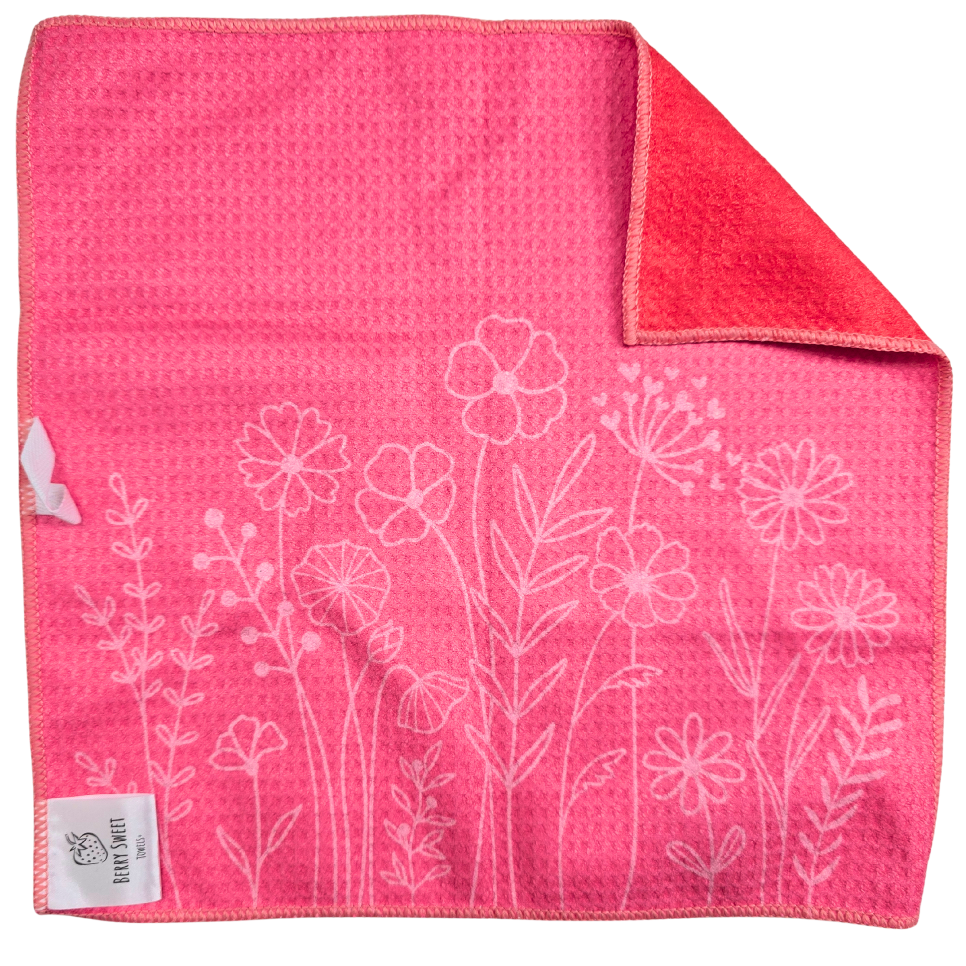 Double-sided waffle weave microfiber washcloth laid flat, showing the pink reverse side with a subtle floral line pattern and a folded corner revealing the orange-pink heart patterned front.