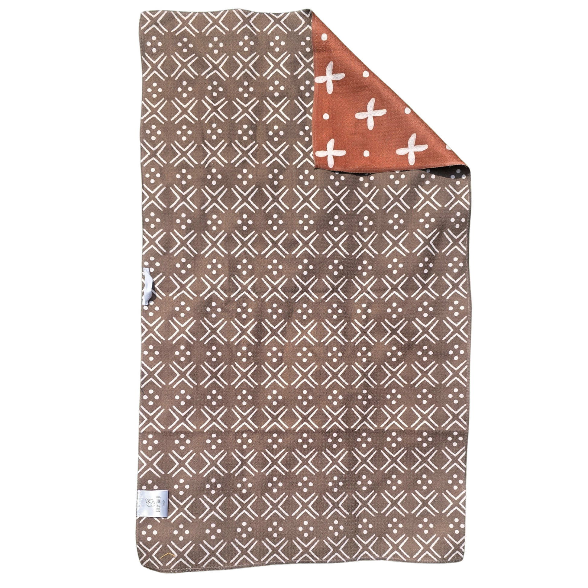 Full view of a double-sided waffle weave microfiber hand towel with dark brown with white geometric patterned side facing up and folded corner showing rust-colored reverse with white cross and dot pattern.
