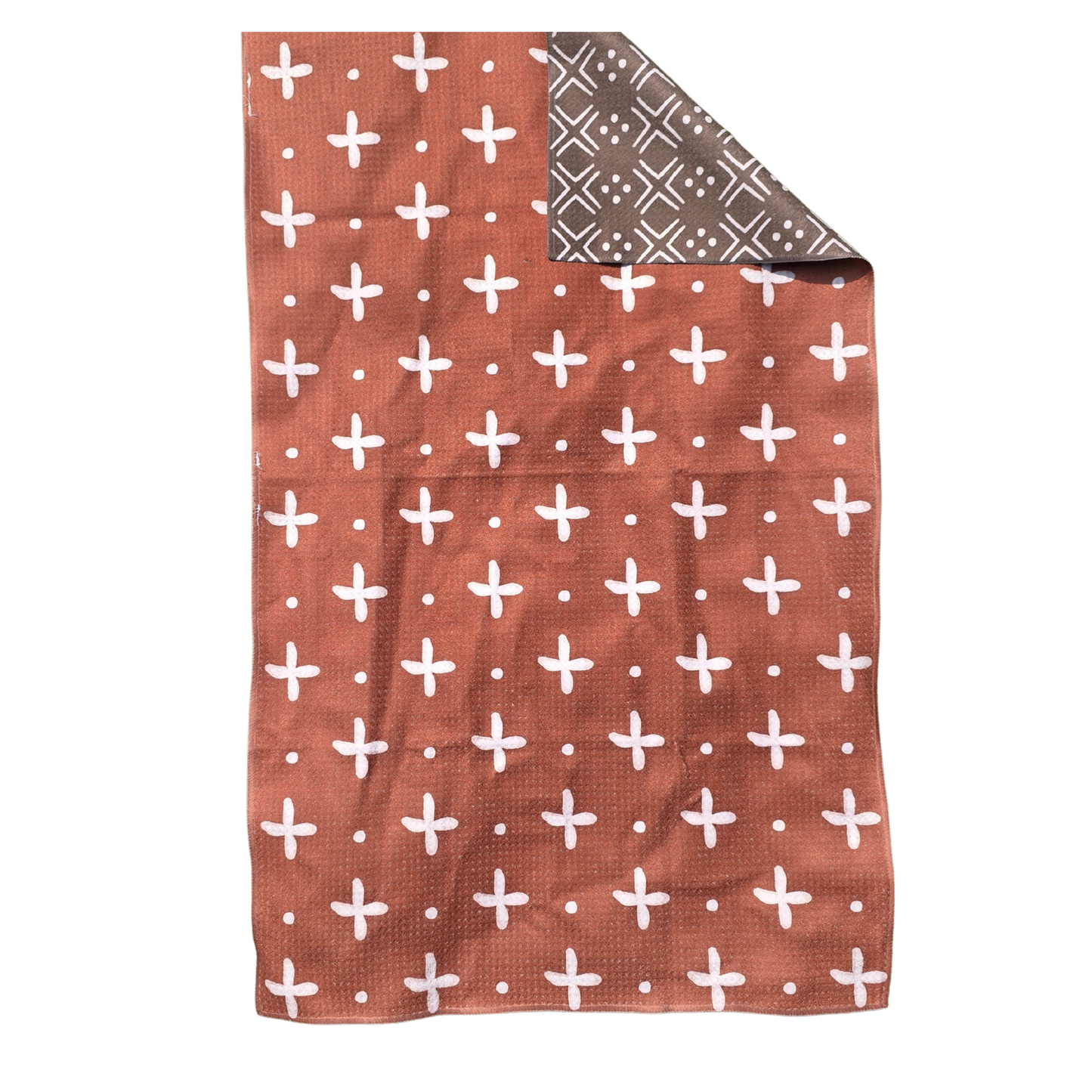 Full view of a double-sided waffle weave microfiber hand towel with rust-colored front featuring white cross and dot pattern and folded corner showing dark brown with white geometric design reverse side.