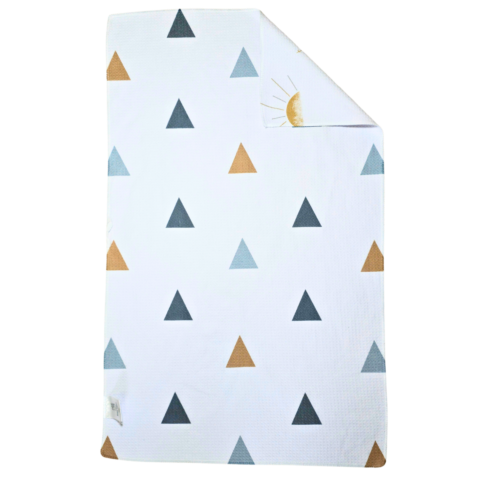 Reverse side of a double-sided microfiber hand towel, displaying a white background with scattered geometric triangle designs in muted blue, gray, and gold with a corner folded over to show the white front with a white and gray sun pattern.