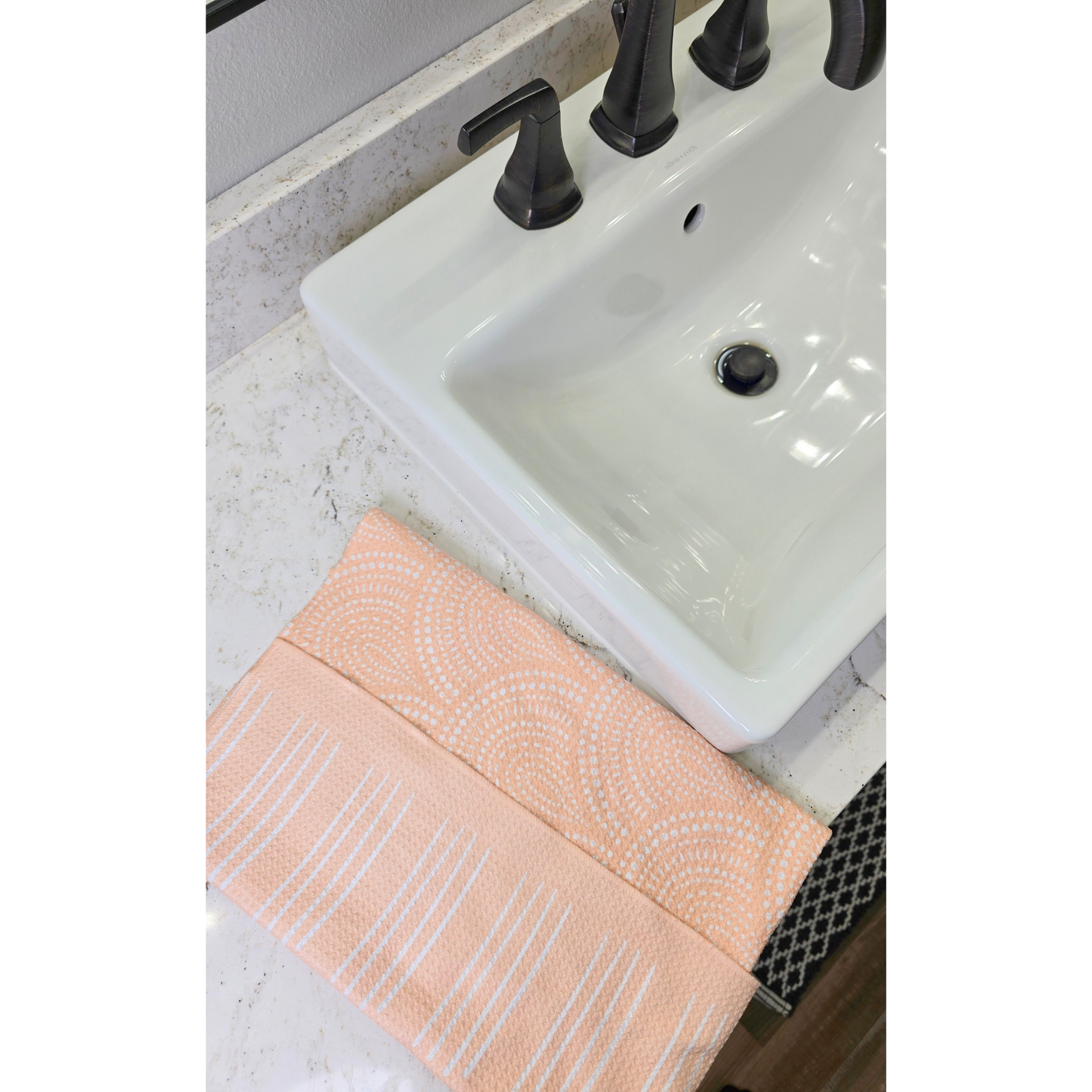 Soft yellow waffle weave microfiber hand towel folded on counter next to a bathroom sink, showing the front side with white linear stripe patterns and the reverse side with a white scalloped geometric design.